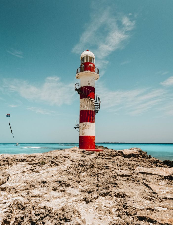 Stunning view of Cancun's red and white lighthouse against a clear blue sky.